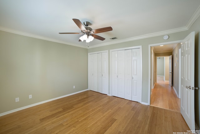 unfurnished bedroom with light wood-type flooring, multiple closets, crown molding, and ceiling fan