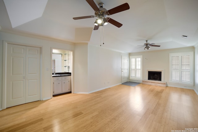 unfurnished living room featuring light hardwood / wood-style flooring, sink, crown molding, a raised ceiling, and ceiling fan