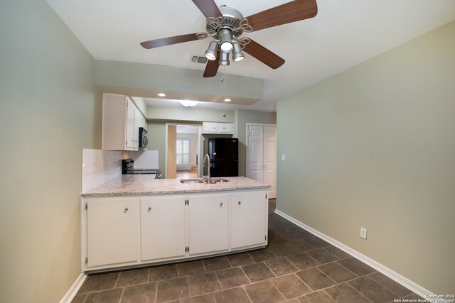 kitchen with dark tile patterned floors, white cabinetry, sink, black fridge, and ceiling fan