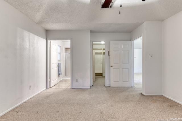 unfurnished bedroom featuring a textured ceiling, ceiling fan, a spacious closet, and ensuite bathroom