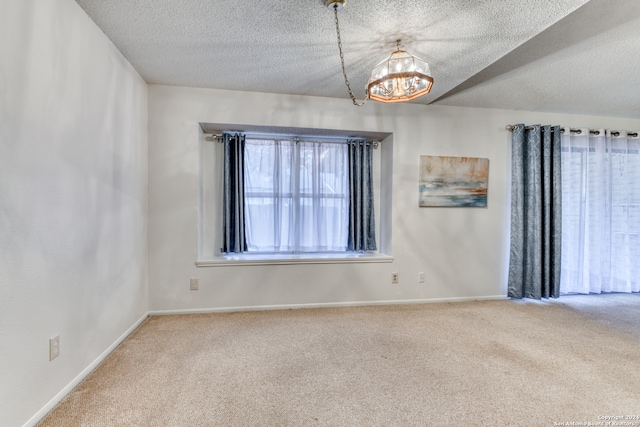 carpeted spare room with a textured ceiling and a notable chandelier