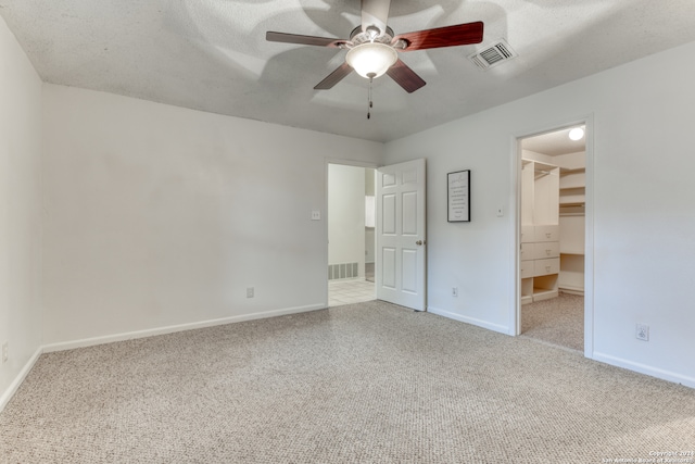 unfurnished bedroom featuring a walk in closet, ceiling fan, a closet, and carpet floors