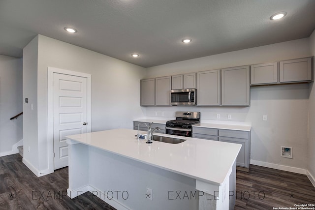 kitchen featuring dark wood-type flooring, appliances with stainless steel finishes, sink, and a kitchen island with sink