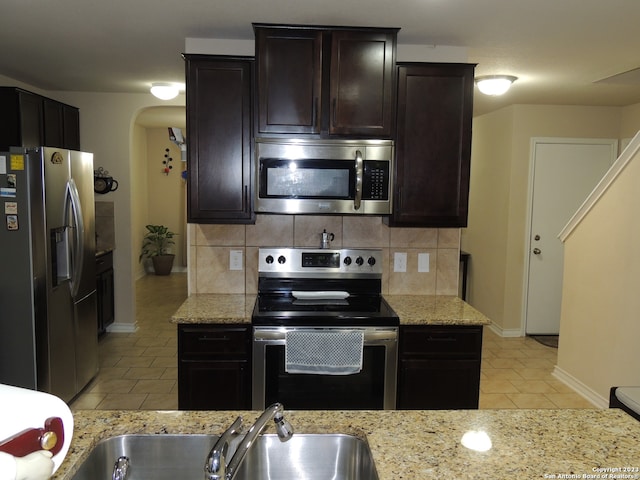 kitchen featuring light tile patterned floors, appliances with stainless steel finishes, light stone counters, and backsplash