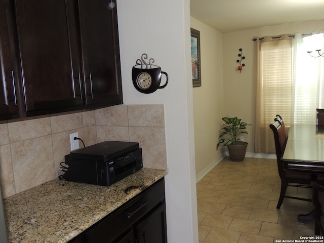 kitchen featuring light tile patterned floors, dark brown cabinetry, decorative backsplash, and light stone countertops