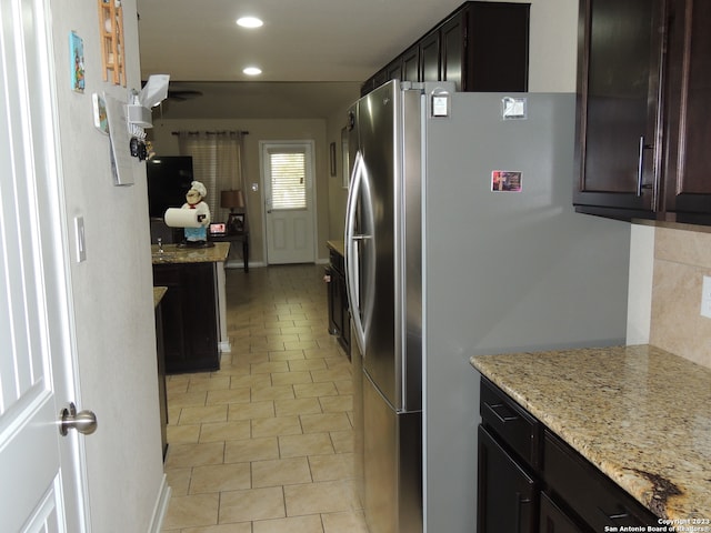 kitchen with tasteful backsplash, light stone counters, stainless steel refrigerator, and light tile patterned floors