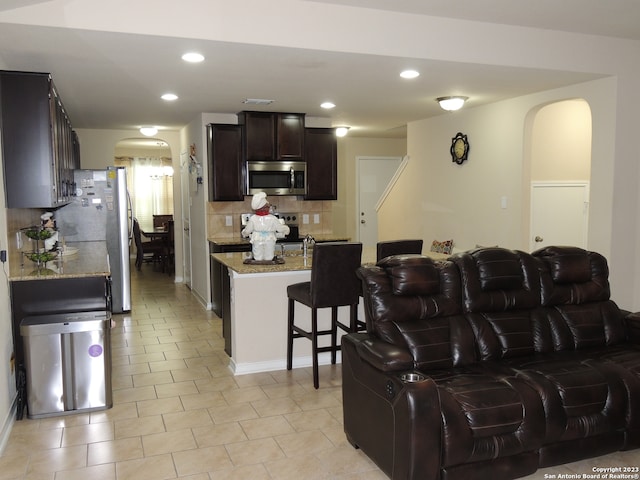 kitchen featuring appliances with stainless steel finishes, decorative backsplash, dark brown cabinetry, light stone counters, and light tile patterned floors