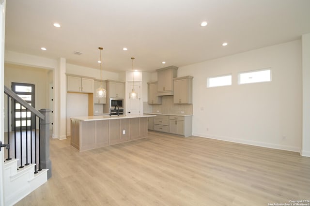 kitchen with sink, stainless steel microwave, light wood-type flooring, pendant lighting, and an island with sink