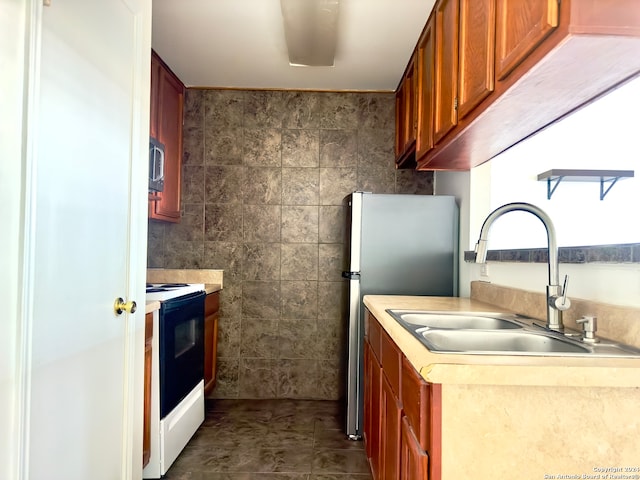 kitchen featuring dark tile patterned floors, stainless steel refrigerator, sink, white range with electric cooktop, and tile walls