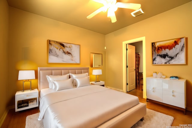 bedroom featuring a ceiling fan, wood finished floors, a walk in closet, baseboards, and visible vents