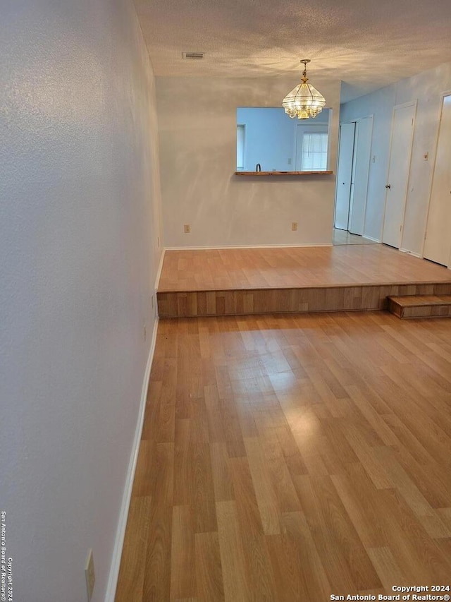 unfurnished dining area featuring a textured ceiling, a chandelier, and hardwood / wood-style flooring