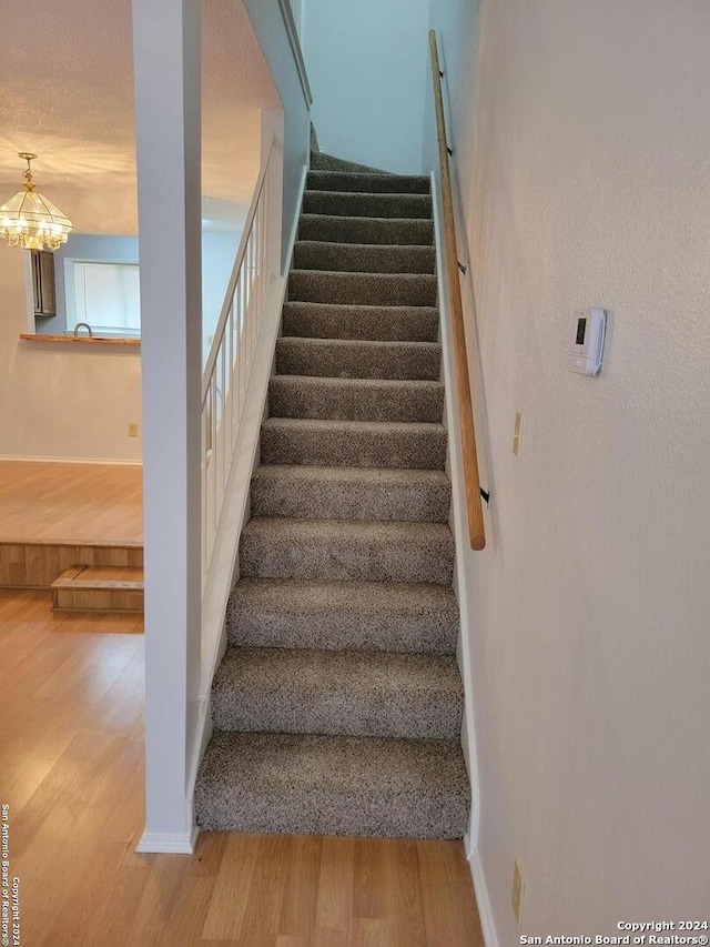 stairway with a textured ceiling, a notable chandelier, and hardwood / wood-style floors