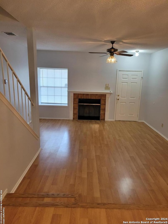 unfurnished living room with light hardwood / wood-style floors, ceiling fan, a textured ceiling, and a fireplace