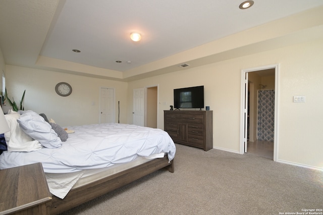 bedroom with a raised ceiling, light colored carpet, and ensuite bathroom