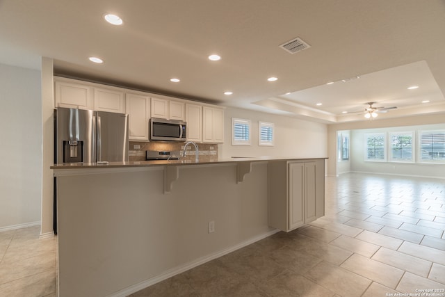 kitchen featuring stainless steel appliances, a raised ceiling, light tile patterned floors, and tasteful backsplash