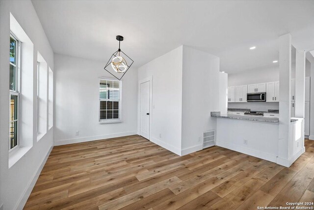 kitchen featuring hanging light fixtures, an inviting chandelier, light wood-type flooring, stainless steel appliances, and white cabinets