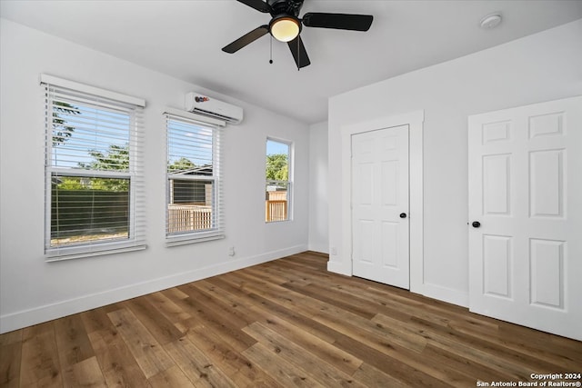 unfurnished bedroom featuring ceiling fan, wood-type flooring, and a wall mounted air conditioner