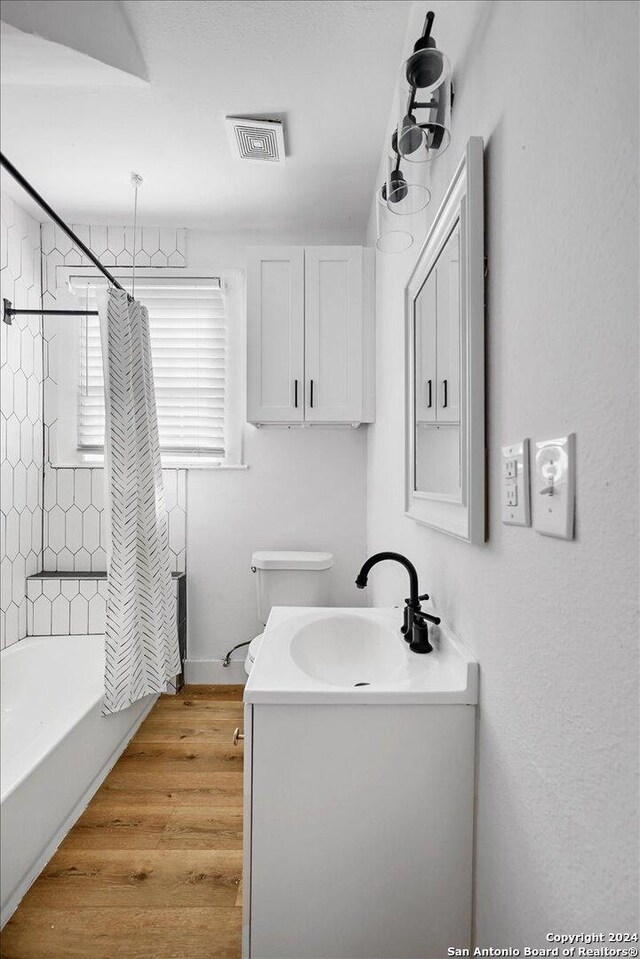 full bathroom featuring wood-type flooring, toilet, shower / tub combo with curtain, and vanity