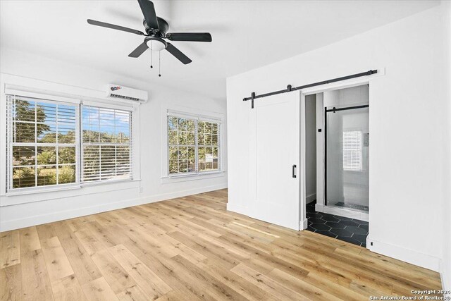 unfurnished bedroom with ceiling fan, a barn door, light hardwood / wood-style flooring, and an AC wall unit