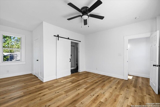 unfurnished bedroom with light hardwood / wood-style flooring, ceiling fan, and a barn door