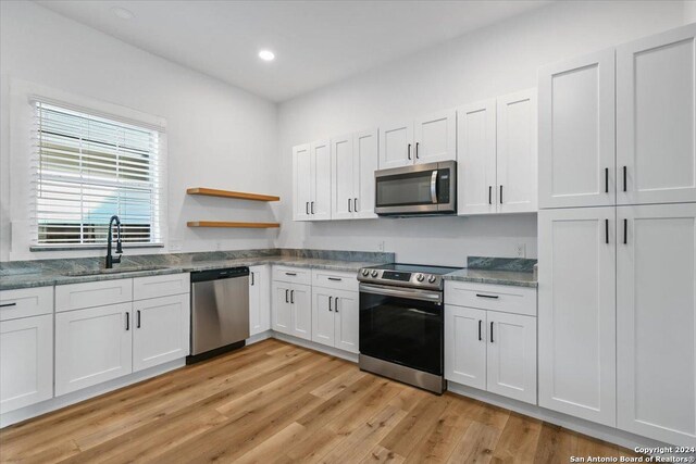 kitchen featuring sink, light stone counters, light hardwood / wood-style floors, stainless steel appliances, and white cabinets