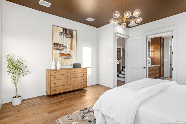 bedroom featuring a notable chandelier, hardwood / wood-style floors, and connected bathroom