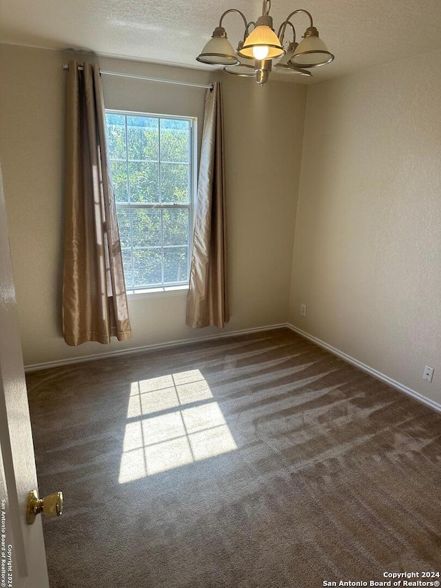 empty room with carpet floors, a textured ceiling, and a chandelier