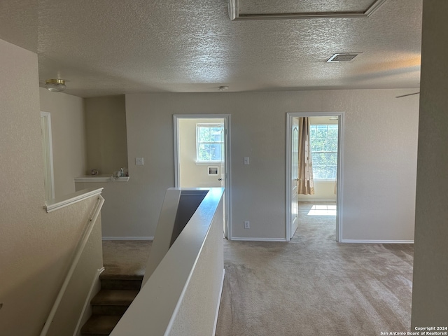 hallway with light carpet, plenty of natural light, and a textured ceiling