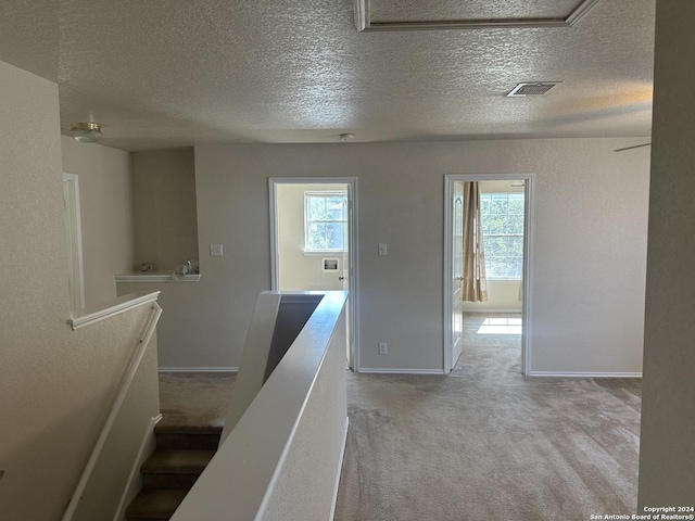 corridor with light carpet, visible vents, an upstairs landing, and baseboards