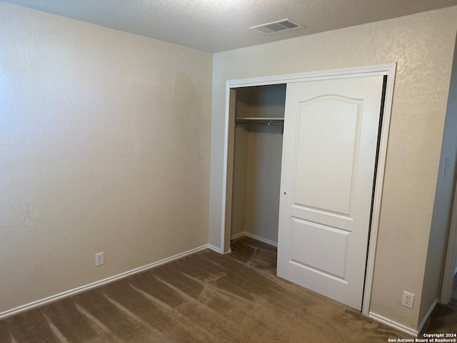 unfurnished bedroom featuring a textured ceiling, a closet, and dark carpet