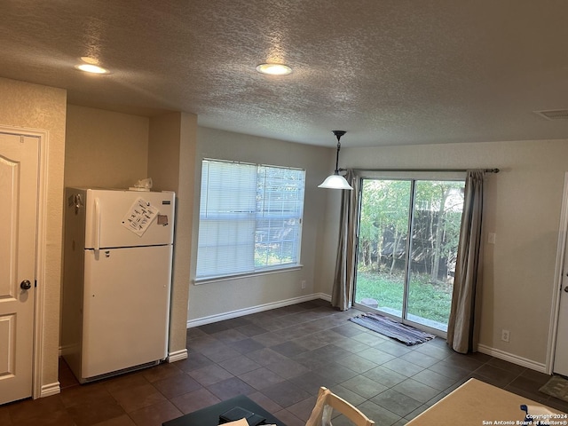 interior space featuring decorative light fixtures, visible vents, freestanding refrigerator, a textured ceiling, and baseboards