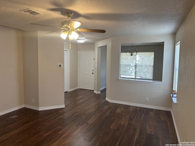 unfurnished room with a textured ceiling, ceiling fan with notable chandelier, visible vents, baseboards, and dark wood-style floors