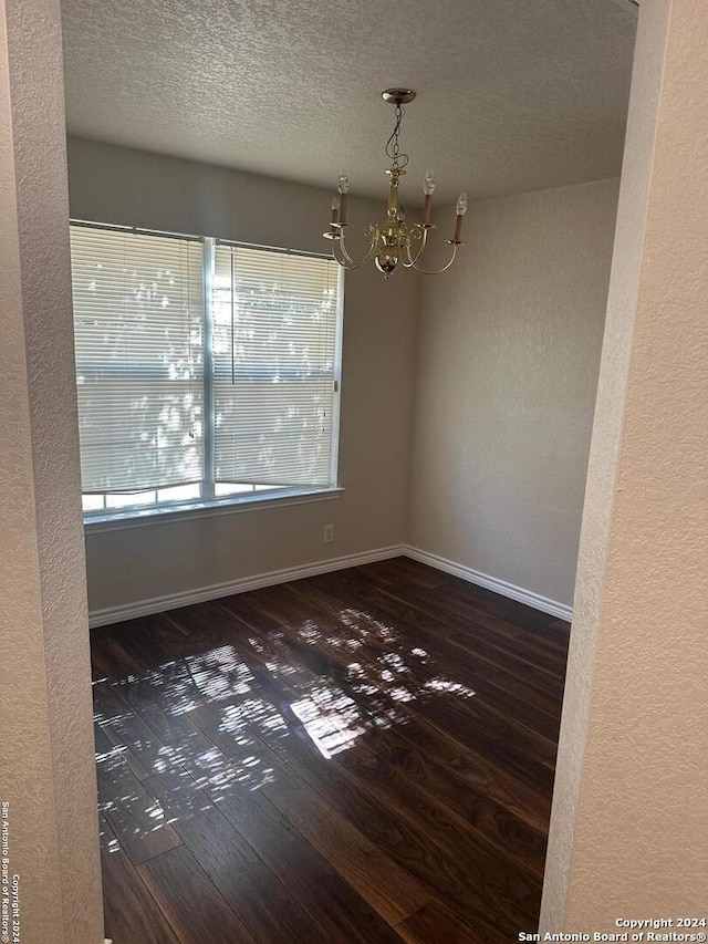 spare room with an inviting chandelier, a textured ceiling, and dark hardwood / wood-style flooring