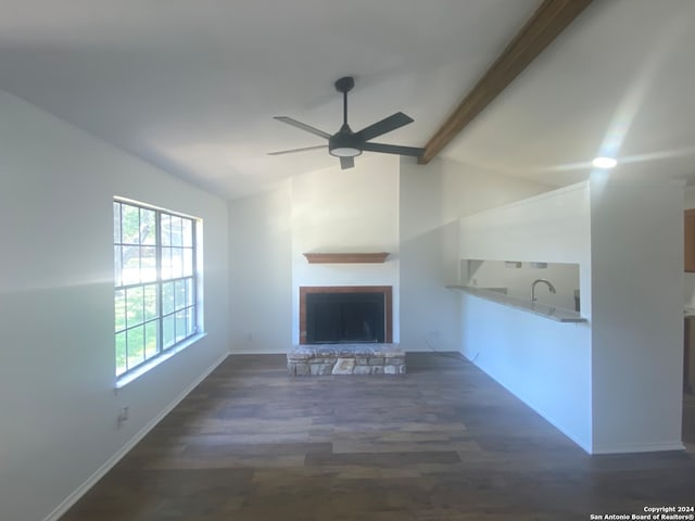 unfurnished living room with ceiling fan, sink, a stone fireplace, lofted ceiling with beams, and dark hardwood / wood-style floors