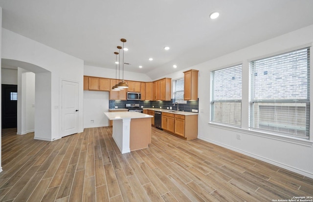 kitchen with arched walkways, light countertops, appliances with stainless steel finishes, a center island, and pendant lighting