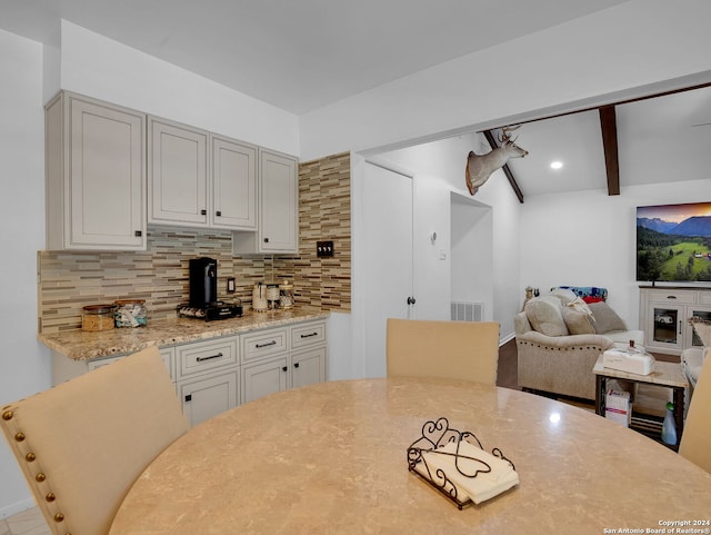 kitchen featuring beam ceiling, light stone countertops, and tasteful backsplash