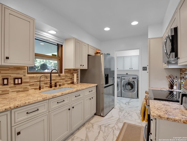 kitchen with sink, light stone countertops, independent washer and dryer, tasteful backsplash, and stainless steel appliances