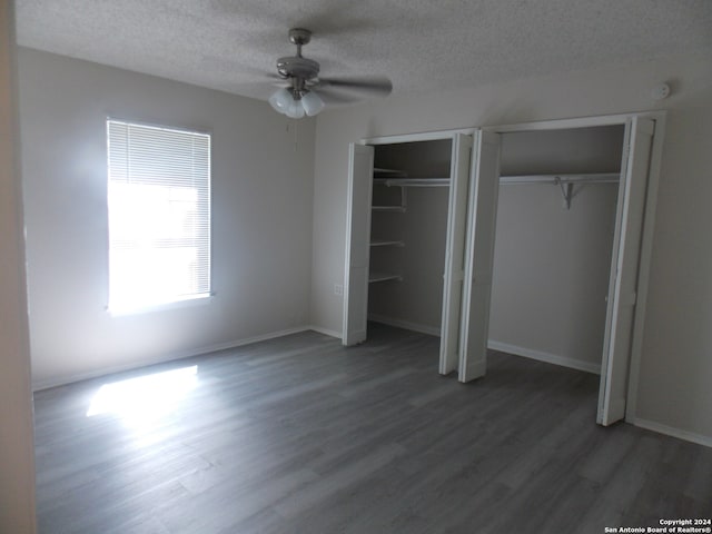 unfurnished bedroom featuring dark wood-type flooring, ceiling fan, a textured ceiling, and multiple closets