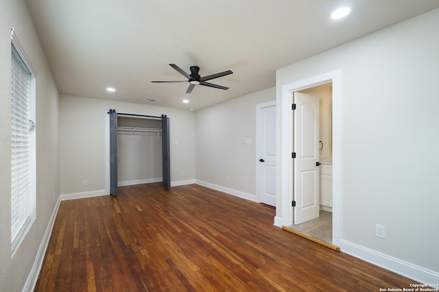 unfurnished bedroom featuring ceiling fan, a barn door, wood-type flooring, a closet, and connected bathroom