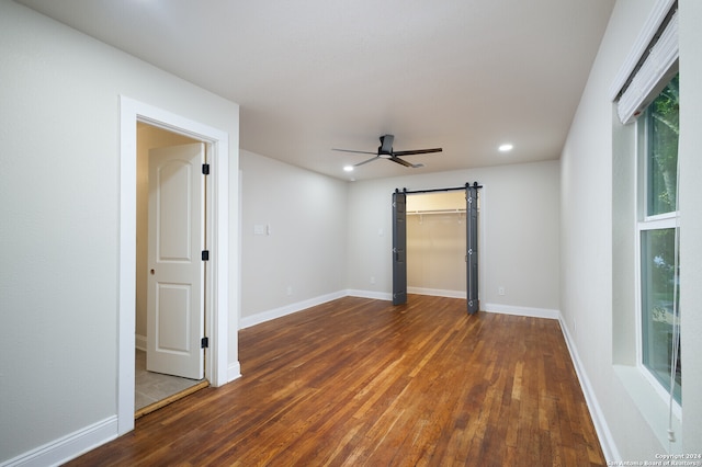 unfurnished room featuring hardwood / wood-style floors, a barn door, and ceiling fan