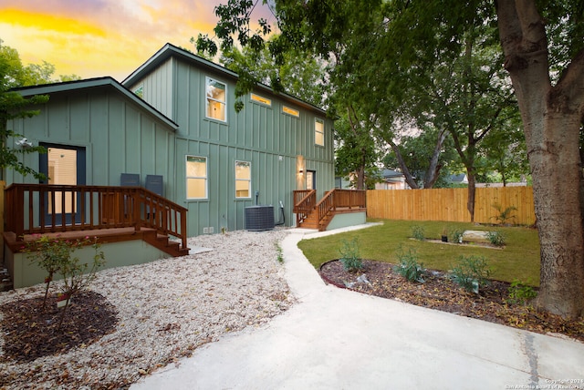 back house at dusk featuring a wooden deck, a yard, and central AC