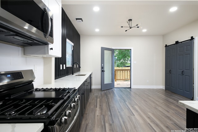 kitchen featuring appliances with stainless steel finishes, sink, white cabinets, wood-type flooring, and a barn door