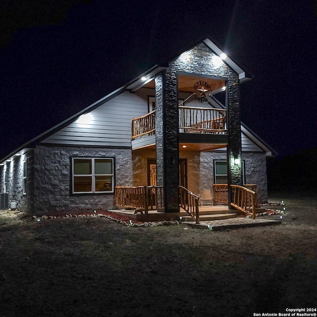 136 Cardinal Dr, Camp Wood, TX 78833 - back of house at night featuring cooling unit, stone siding, and a balcony