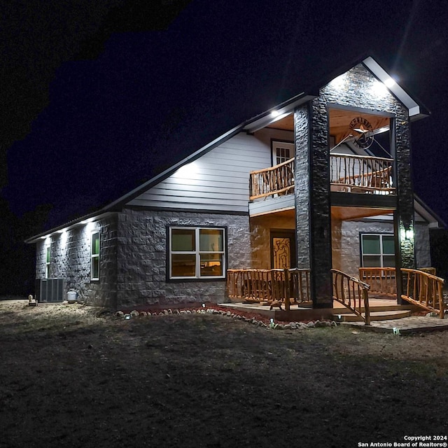 136 Cardinal Dr, Camp Wood, TX 78833 - back of house at night featuring a balcony, cooling unit, and stone siding