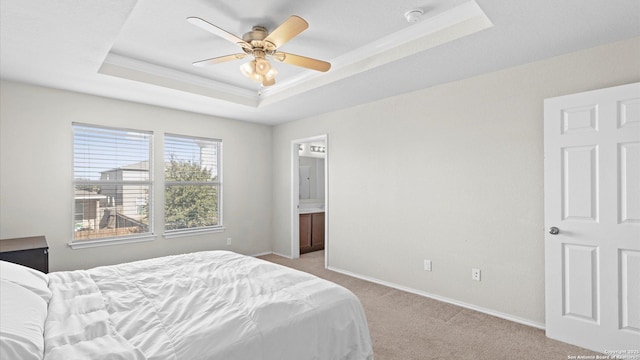 bedroom featuring a raised ceiling, light colored carpet, connected bathroom, and baseboards