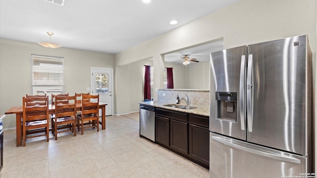 kitchen featuring dark brown cabinetry, a sink, appliances with stainless steel finishes, decorative backsplash, and light stone countertops