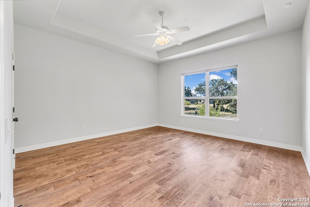 spare room with ceiling fan, light hardwood / wood-style flooring, and a tray ceiling