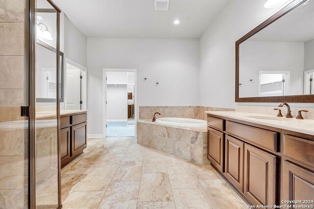 bathroom with tile patterned flooring, a relaxing tiled tub, and vanity