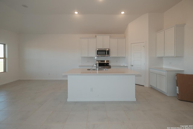 kitchen featuring stainless steel appliances, a sink, white cabinetry, light countertops, and a center island with sink