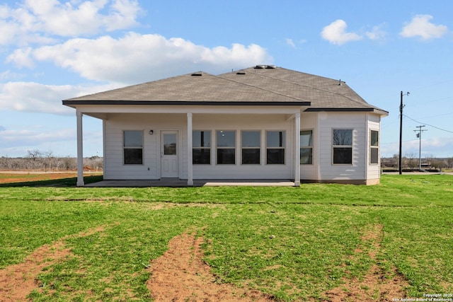 rear view of house with roof with shingles and a lawn